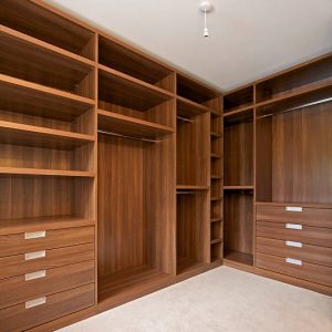 a walk-in wardrobe in a luxury new home ready to fill. Beautifully constructed from walnut with ample shelves, hanging bars and storage space in general.